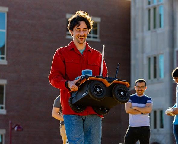 Alumnus and graduate student Ori Miller, carrying a robot that the ARISE lab uses in its research