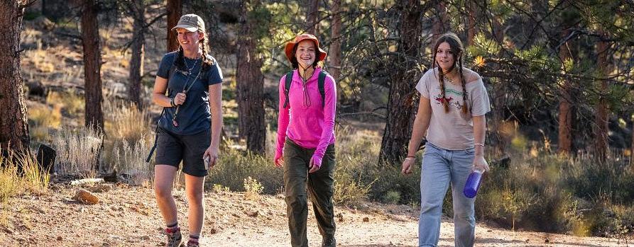 three students hiking through the trees at KMC